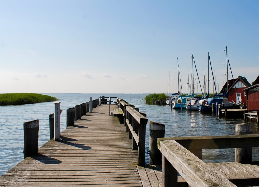 Blick vom Steg auf den Hafen, ein paar Boote und Gebäude.