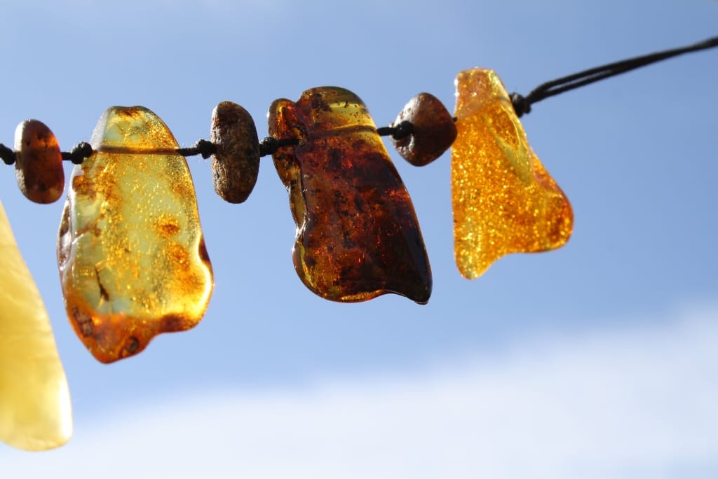 Verschiedene Bernsteine an einer dunklen Schnur vor blauem Himmel.