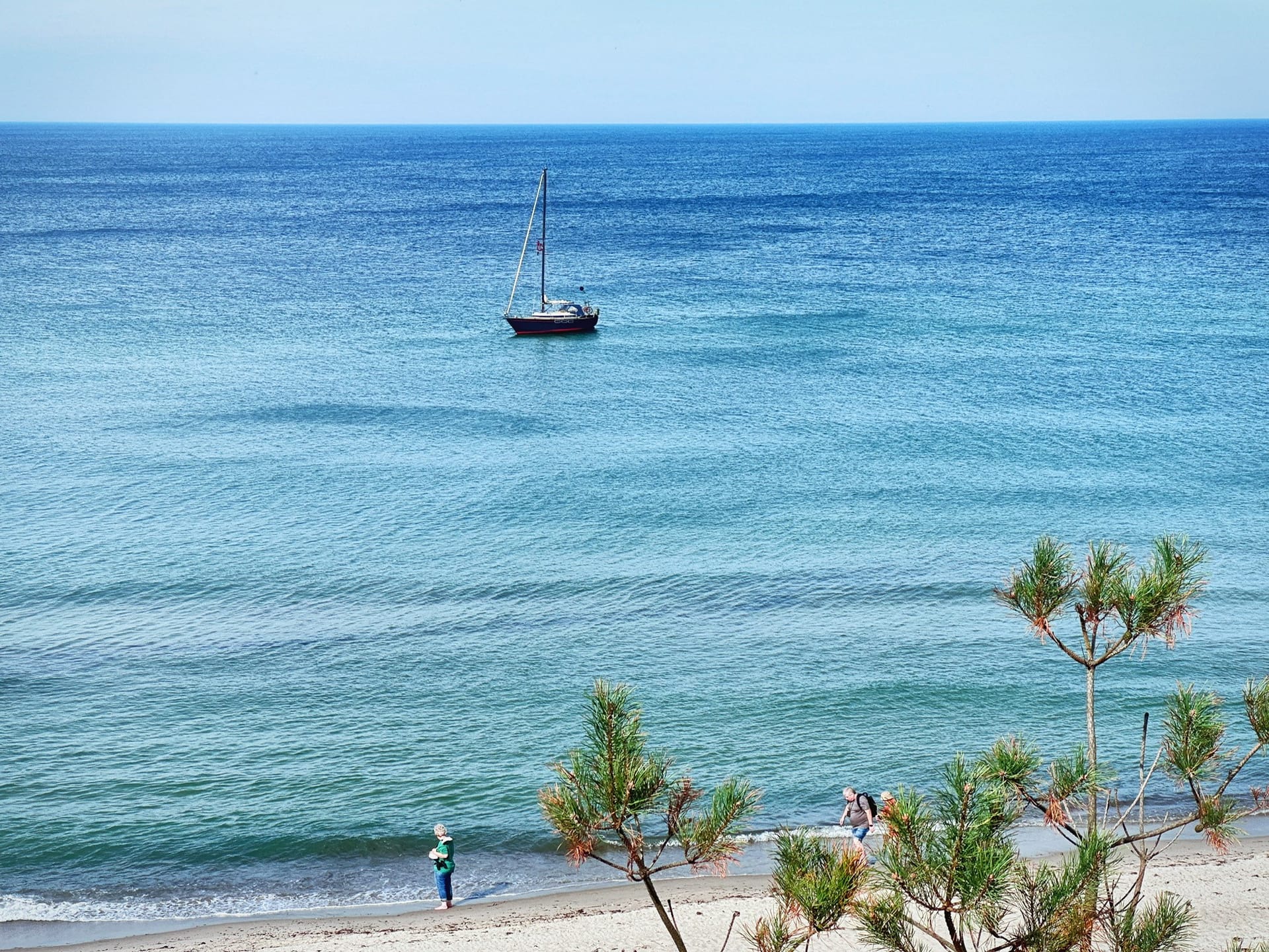 Eine erhöhte Perspektive zeigt das Meer. Im Vordergrund befinden sich Pflanzen. Im mittleren Bereich ist ein kleines Boot auf dem Wasser sichtbar. 