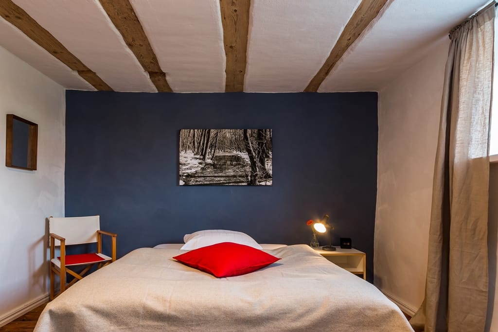 Schlafzimmer mit Doppelbett vor einer dunkelblauen Wand und Decke mit Holzbalken.