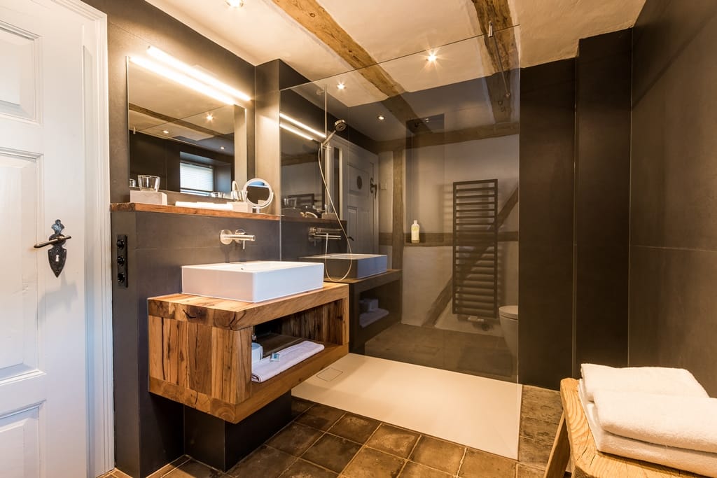 Badezimmer mit dunklen Wänden, Terrakottaboden, Holzwaschtisch und begehbarer Dusche.