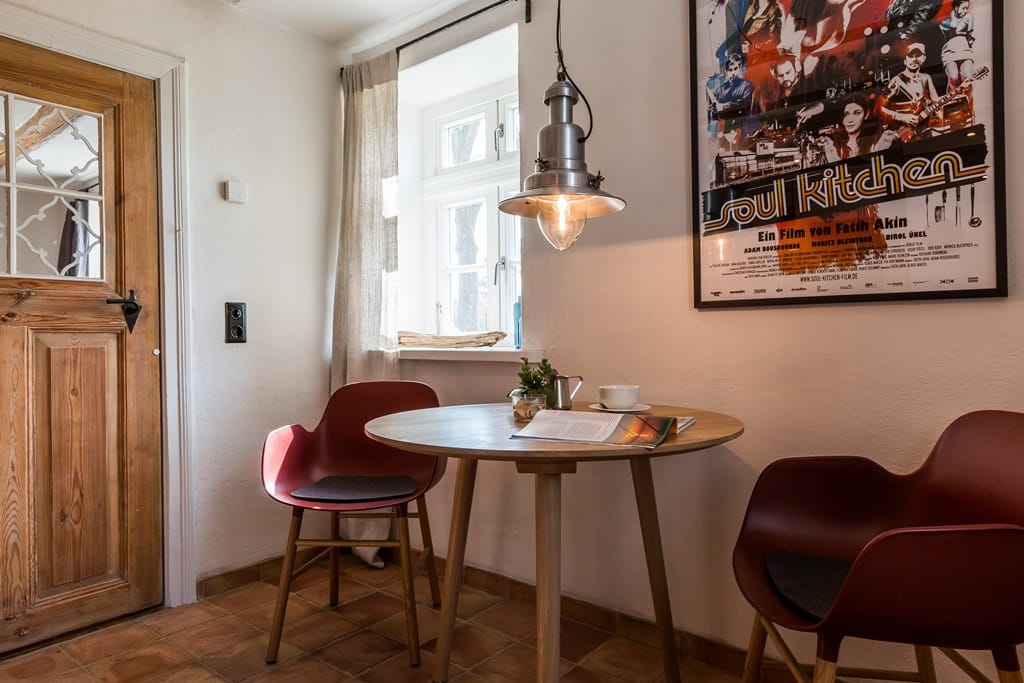 Holztisch mit zwei dunkelroten Stühlen vor einem Fenster und einem Filmplakat an der Wand.