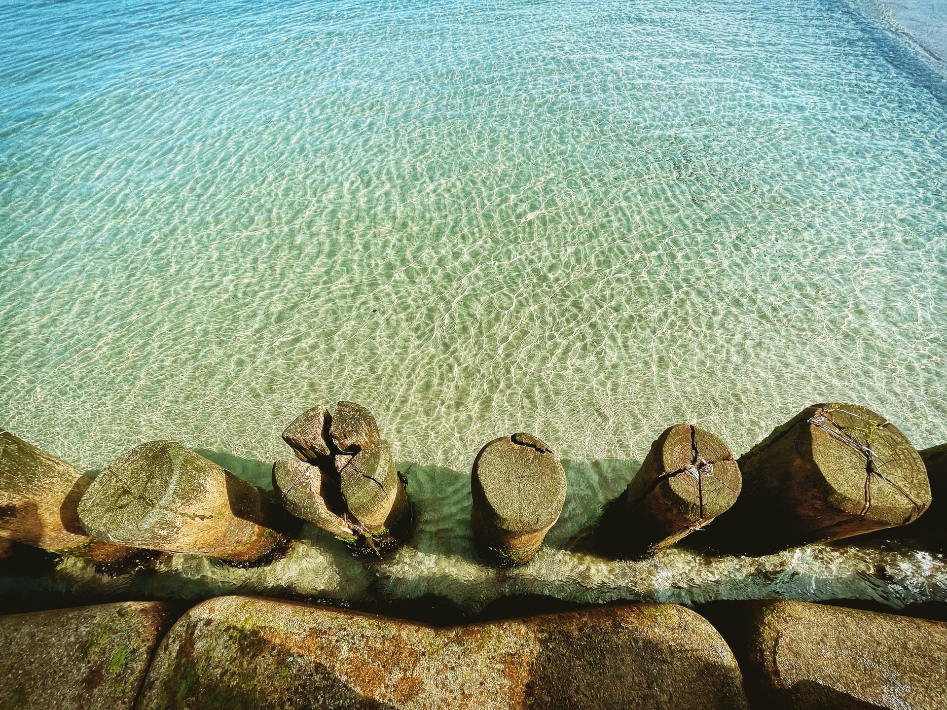 Steine und hölzerne Pfähle als Wellenbrecher und trennen den sandigen Strand vom Meer.