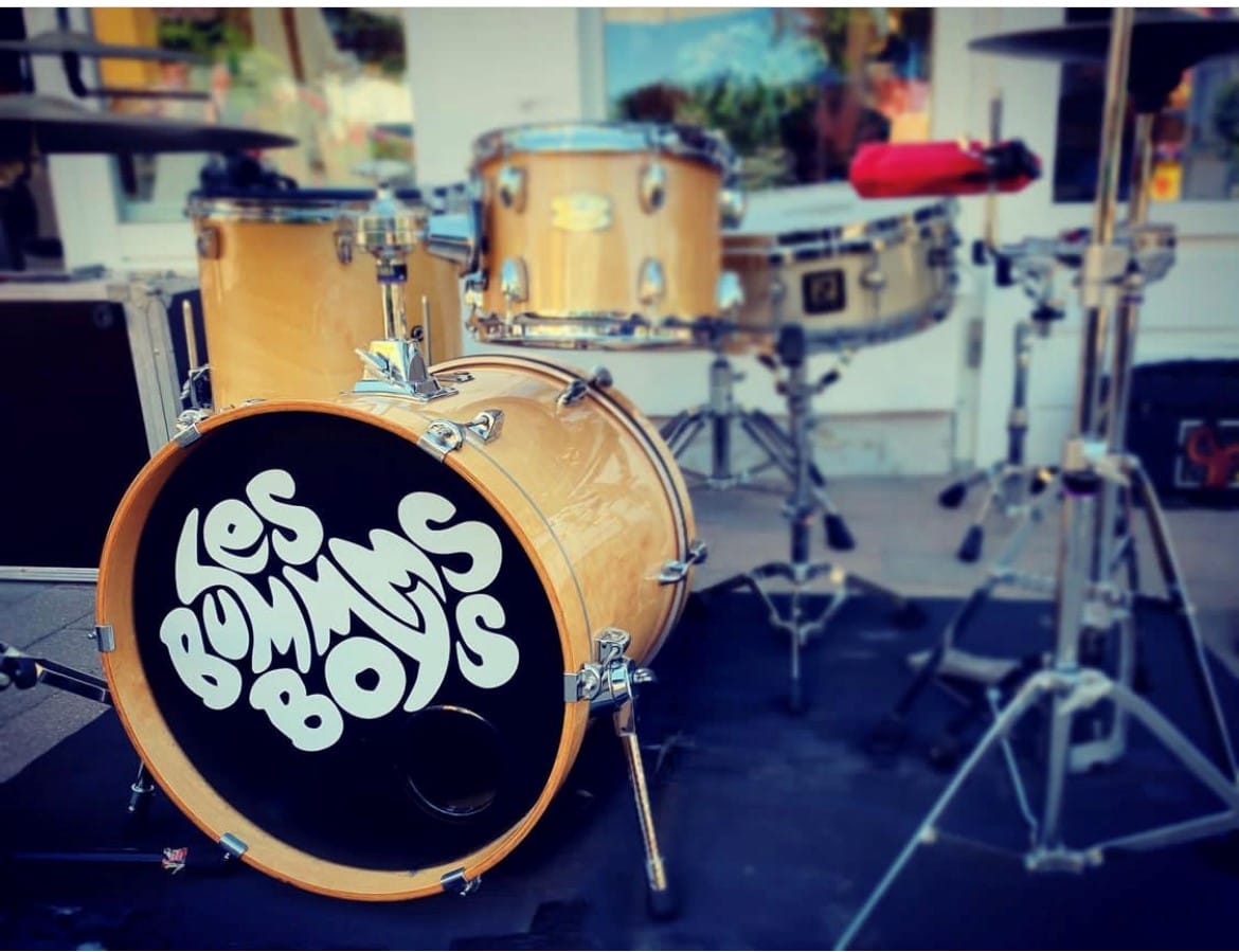 Ein helles Schlagzeug-Set mit einem Band-Logo steht im Freien.