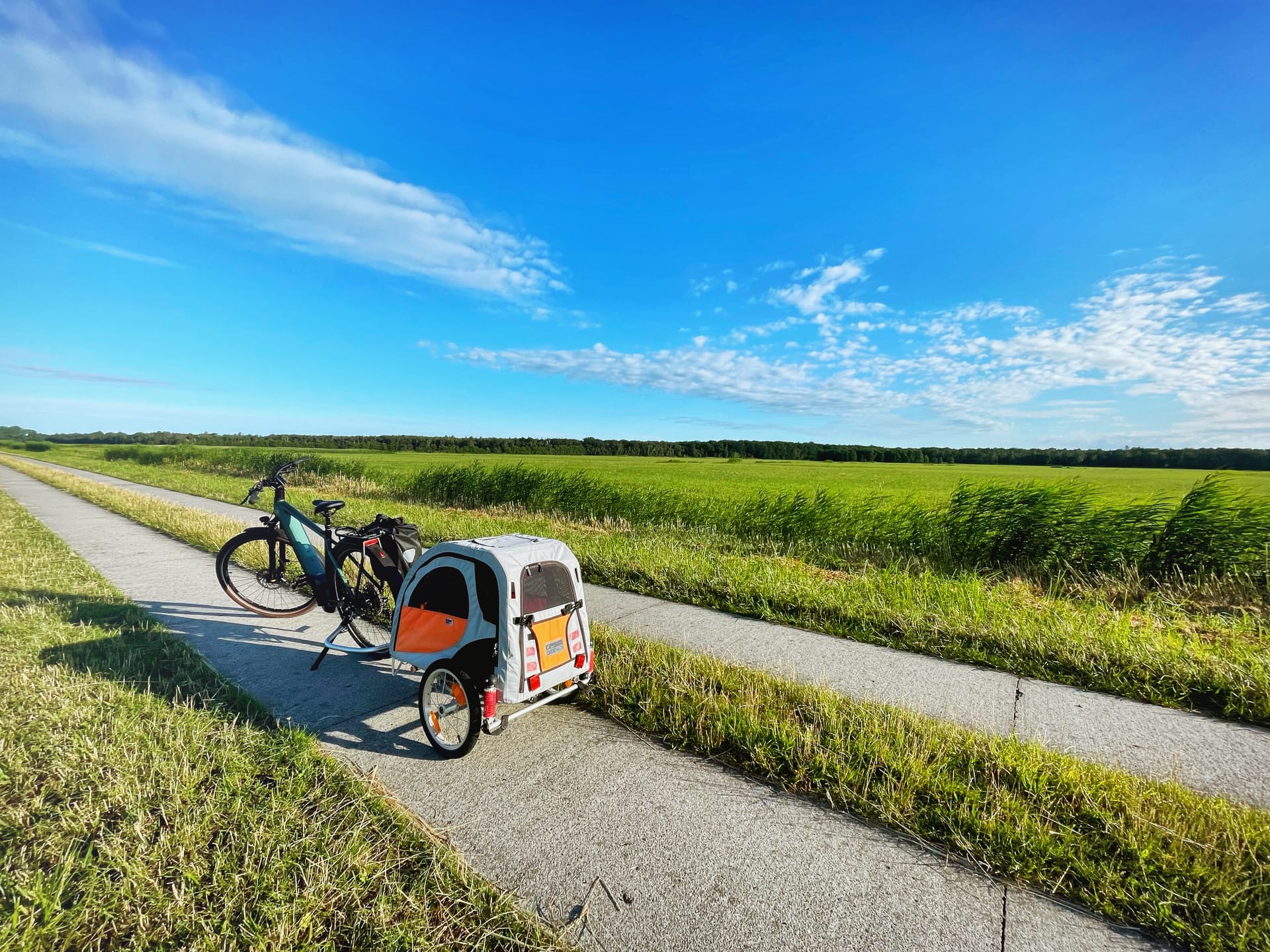 Fahrrad mit Anhänger auf dem Fahrradweg. Grüne Felder und blauer Himmel.