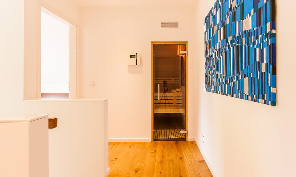 Ein heller Flur mit Holzboden, einer Sauna mit Glastür und einem großformatigen blau-schwarzen Wandbild.