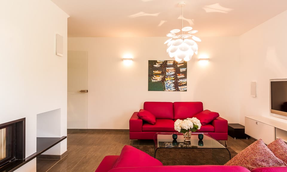 Ein Wohnzimmer mit zwei roten Ledersofas, einem Glastisch vor einem Wandbild und einer hellen Pendelleuchte.