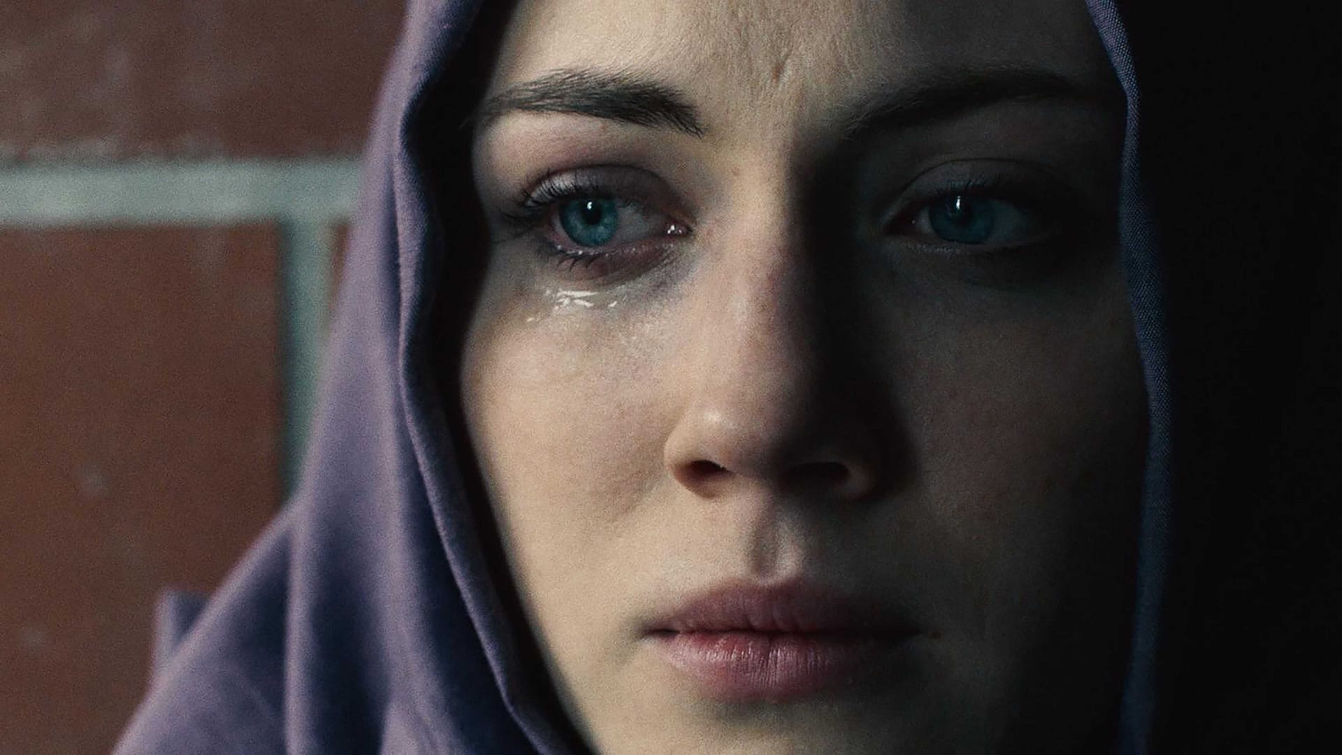 Nahaufnahme eines Frauengesichts. Blaue Augen, Träne auf der Wange. Violettes Kopftuch.