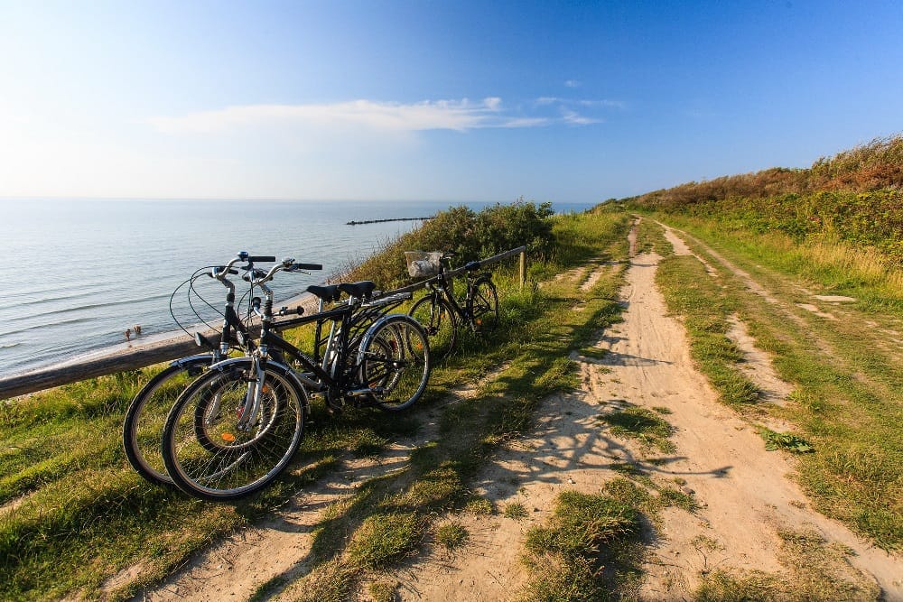 Fahrradweg auf der Steilküste. Fahrräder am Holzzaun abgestellt. Im Hintergrund das Meer und blauer Himmel.