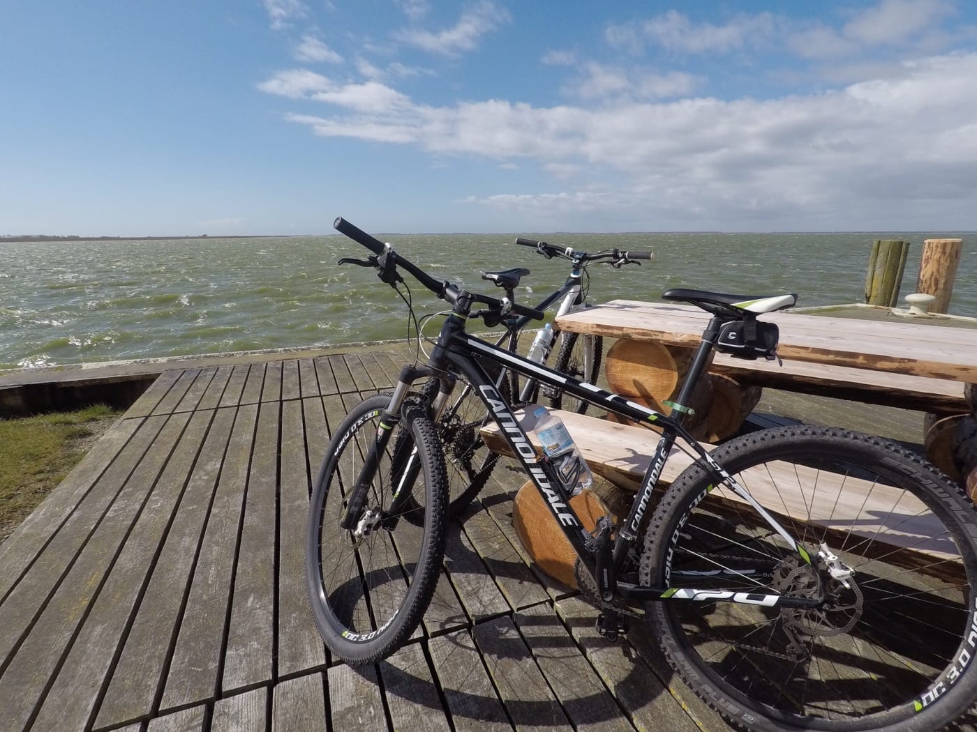 Zwei Fahrräder am Holzsteg neben einer Bank abgestellt. Im Hintergrund Wasser.