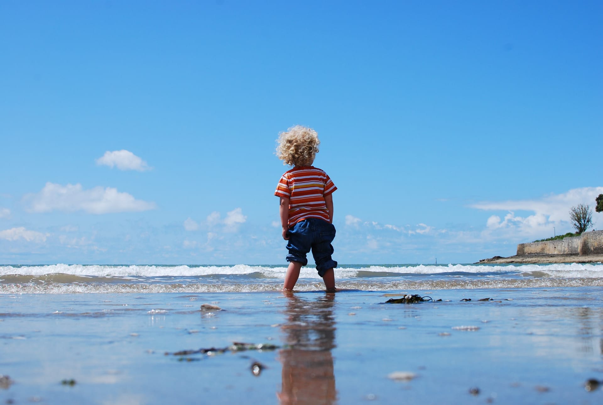 Rückenansicht eines Kindes, das knöcheltief im Meer steht.