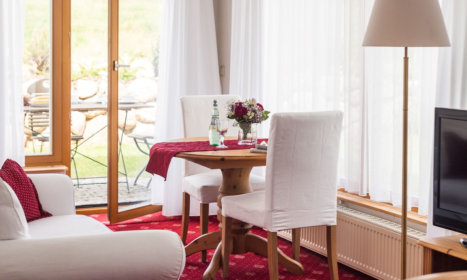 Links ein Sofa, rechts ein Tisch mit zwei Stühlen, eine Lampe und ein Fernseher.
