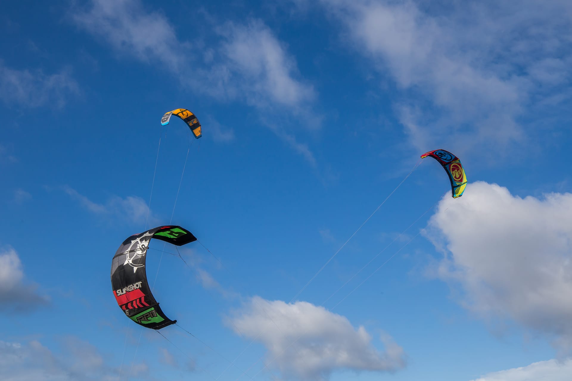 Drei bunte Kites fliegen unter einem blauen Himmel mit weißen Wolken.