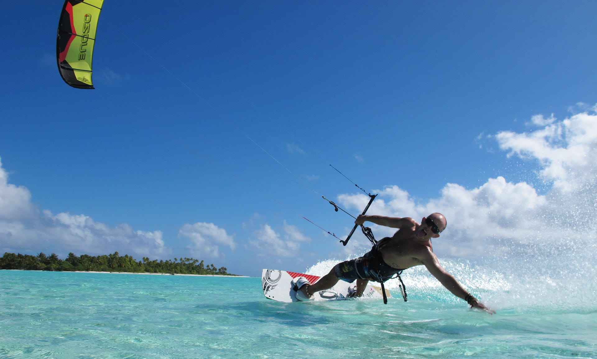 Ein Mann kitesurft auf türkisem Wasser unter blauem Himmel mit einer Insel im Hintergrund.