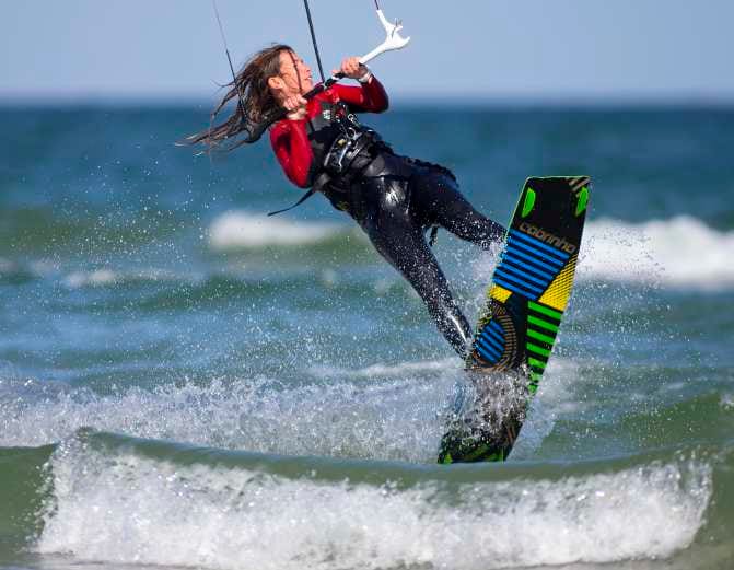 Eine Person kitesurft aktiv auf dem Wasser, umgeben von Wellen und unter einem klaren Himmel.