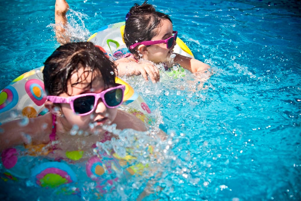 Zwei Kinder mit Sonnenbrillen und Schwimmringen im Pool.