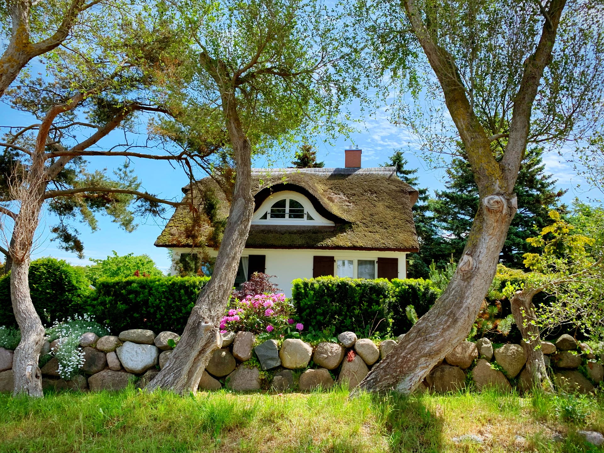 Reetgedecktes Haus im Grünen, umrahmt von Bäumen und blühendem Garten
