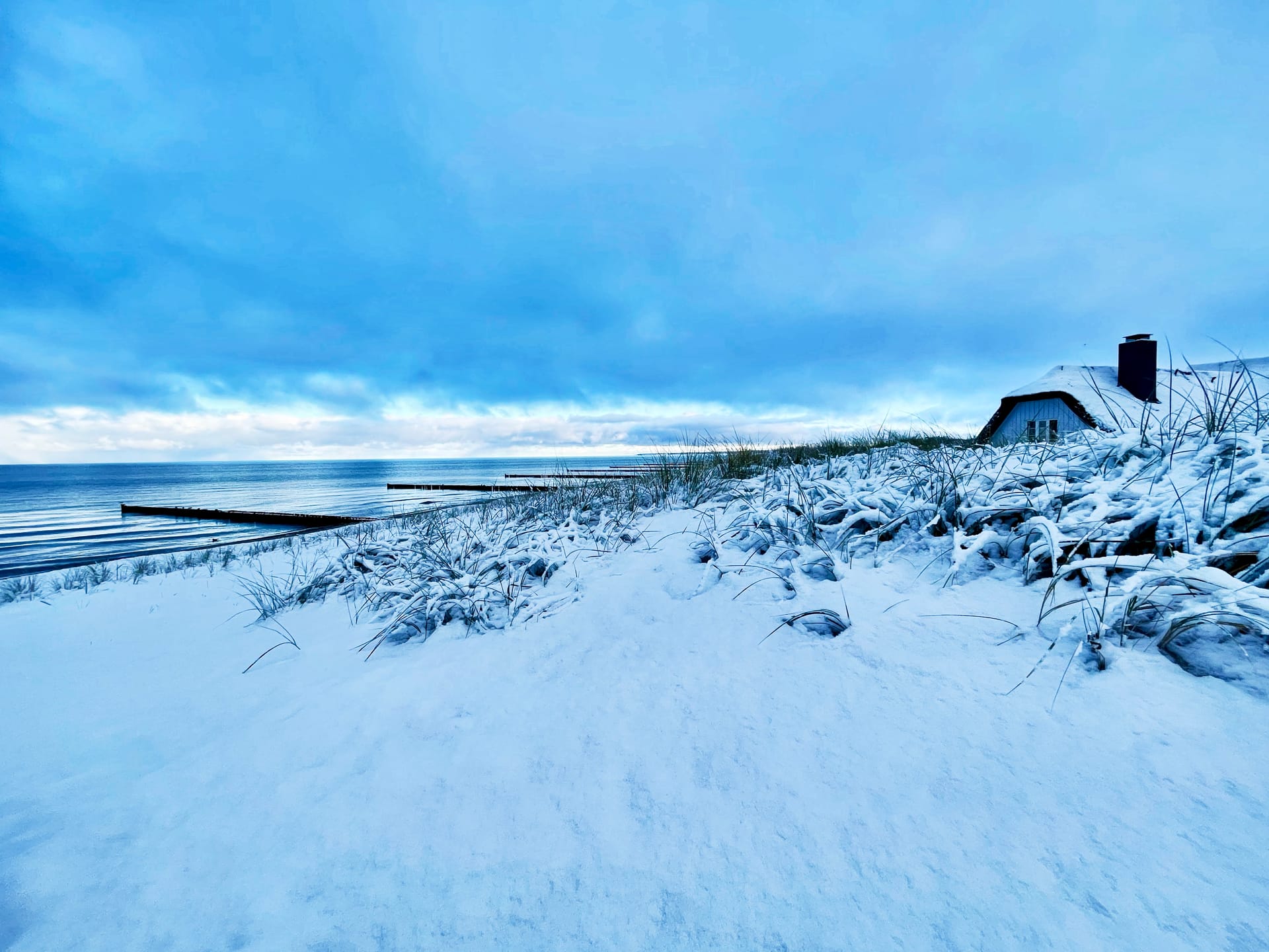 Verschneiter Ostseestrand mit Dünen, Buhnen und Reetdachhaus