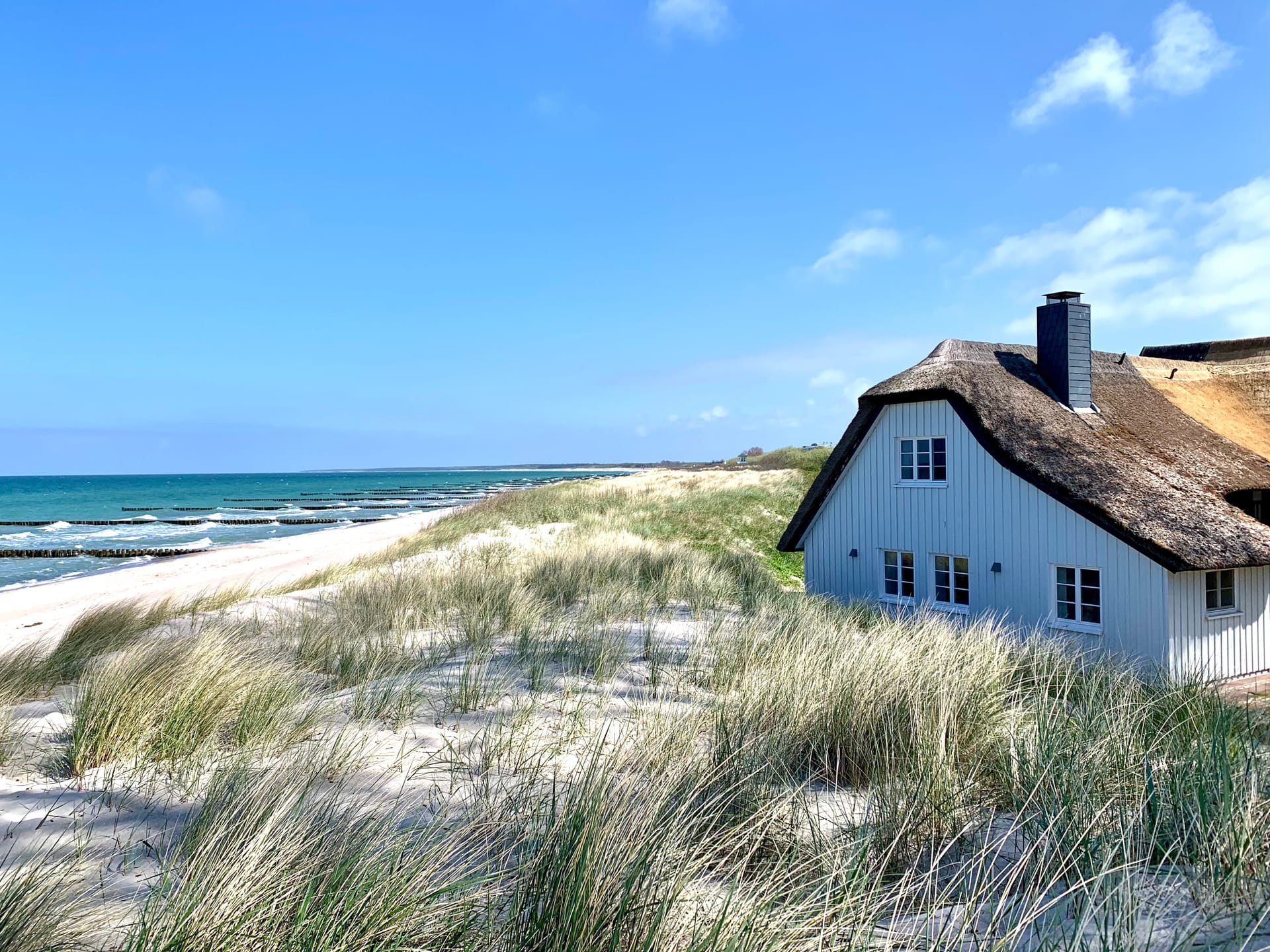Reetdachhaus in den Dünen mit Blick auf Strand und Ostsee unter blauem Himmel