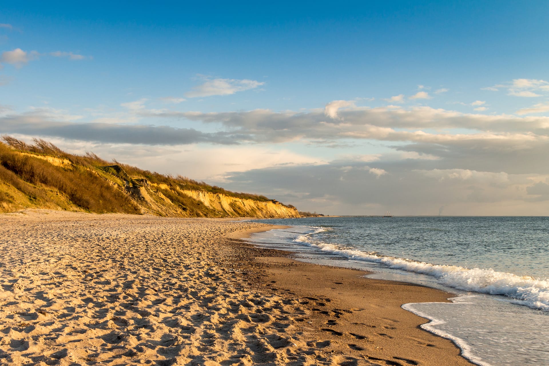 Sandstrand mit sanften Wellen und Steilküste an der Ostsee im warmen Abendlicht