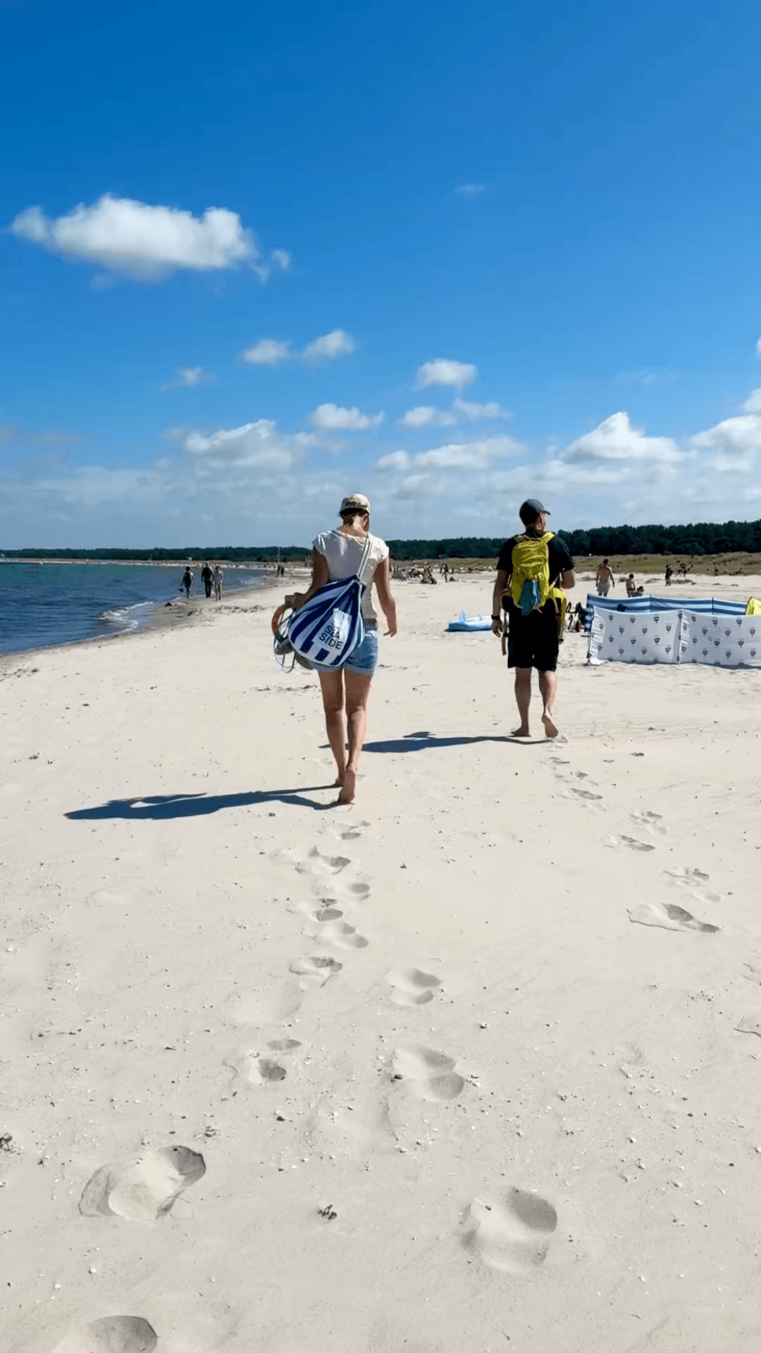 „Zwei Personen gehen barfuß am Ostseestrand entlang, Fußspuren im Sand