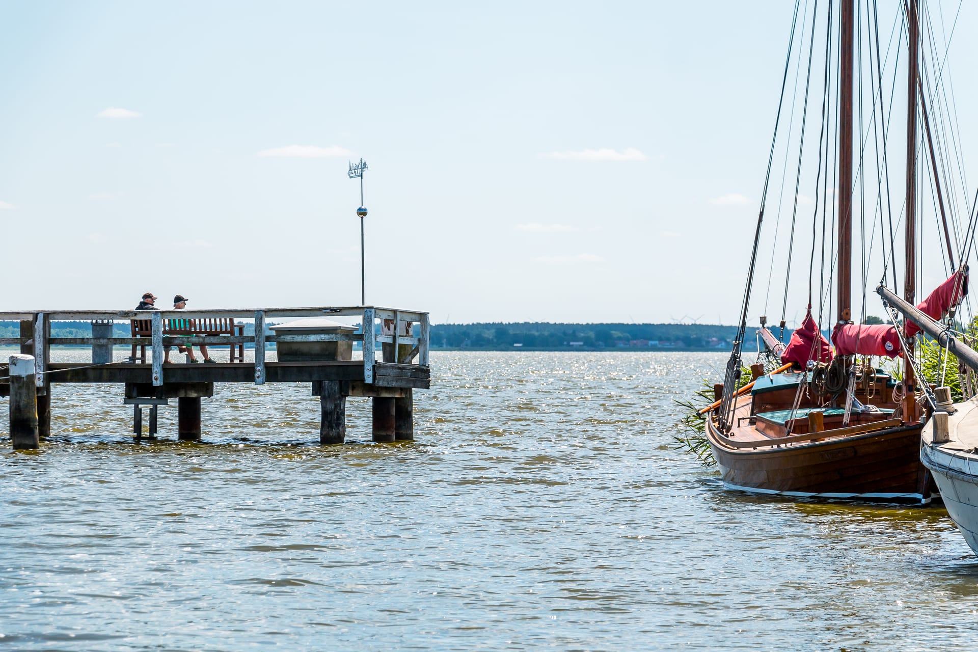 Holzsteg am Bodden mit Bank und traditionellem Segelboot