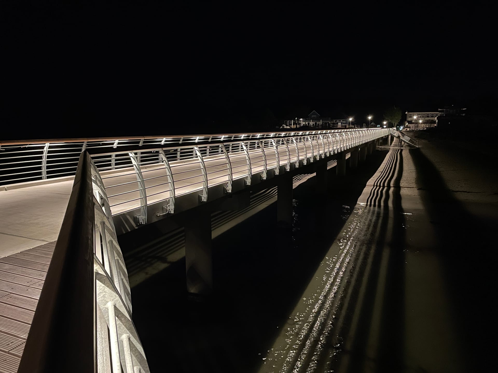 Beleuchtete Seebrücke bei Nacht mit Spiegelungen im Wasser