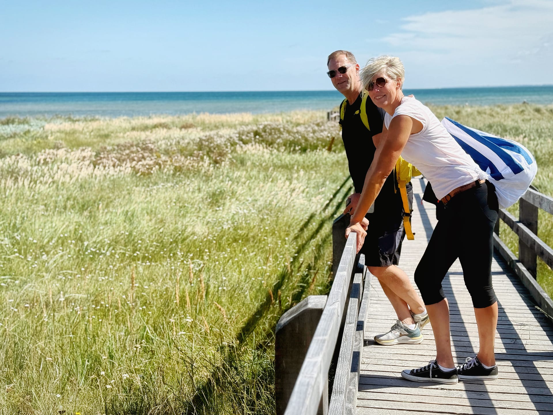 Paar lehnt am Holzsteg und blickt über Dünen und Ostsee