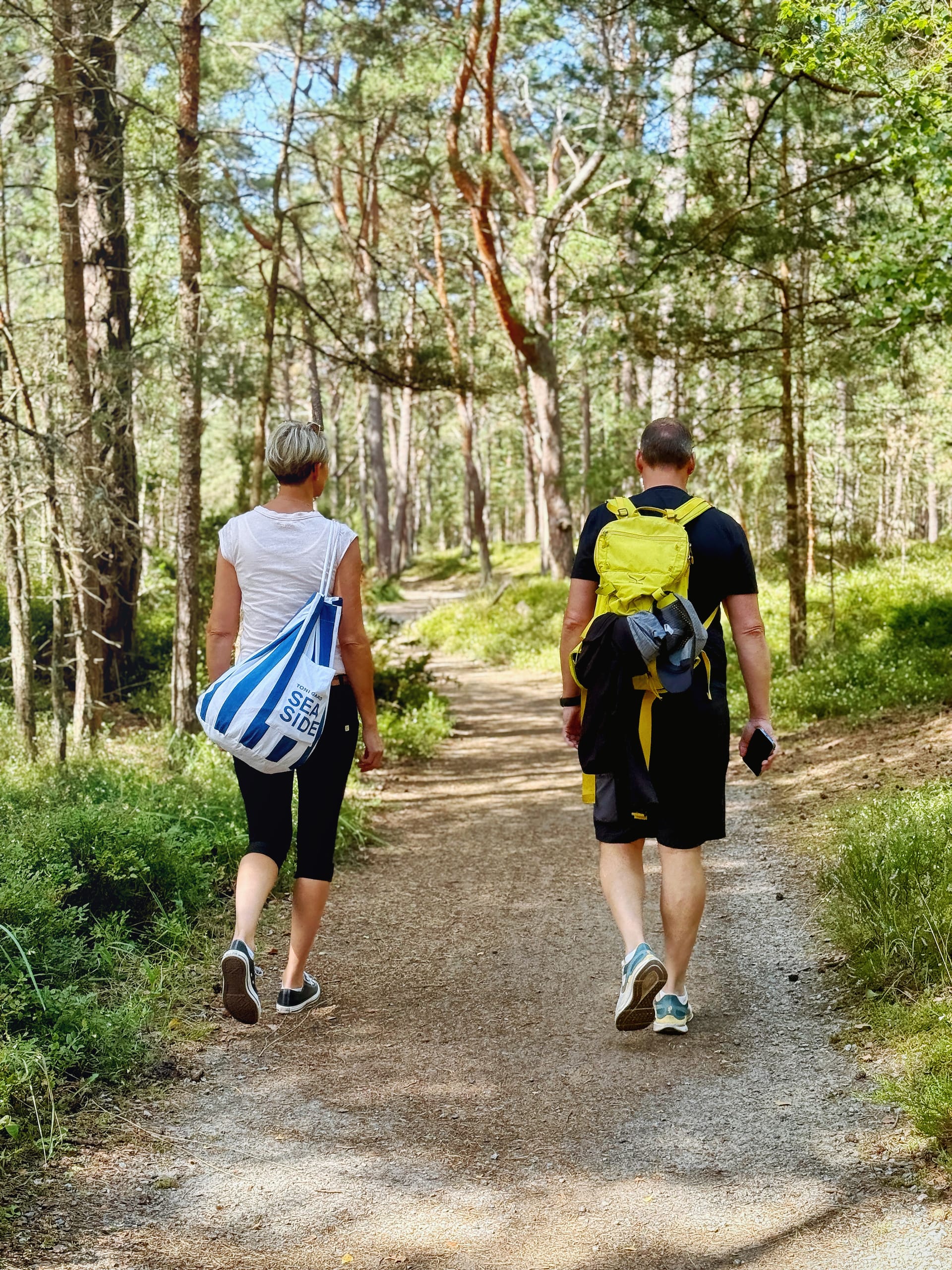 Paar wandert entspannt auf Waldweg durch lichten Kiefernwald