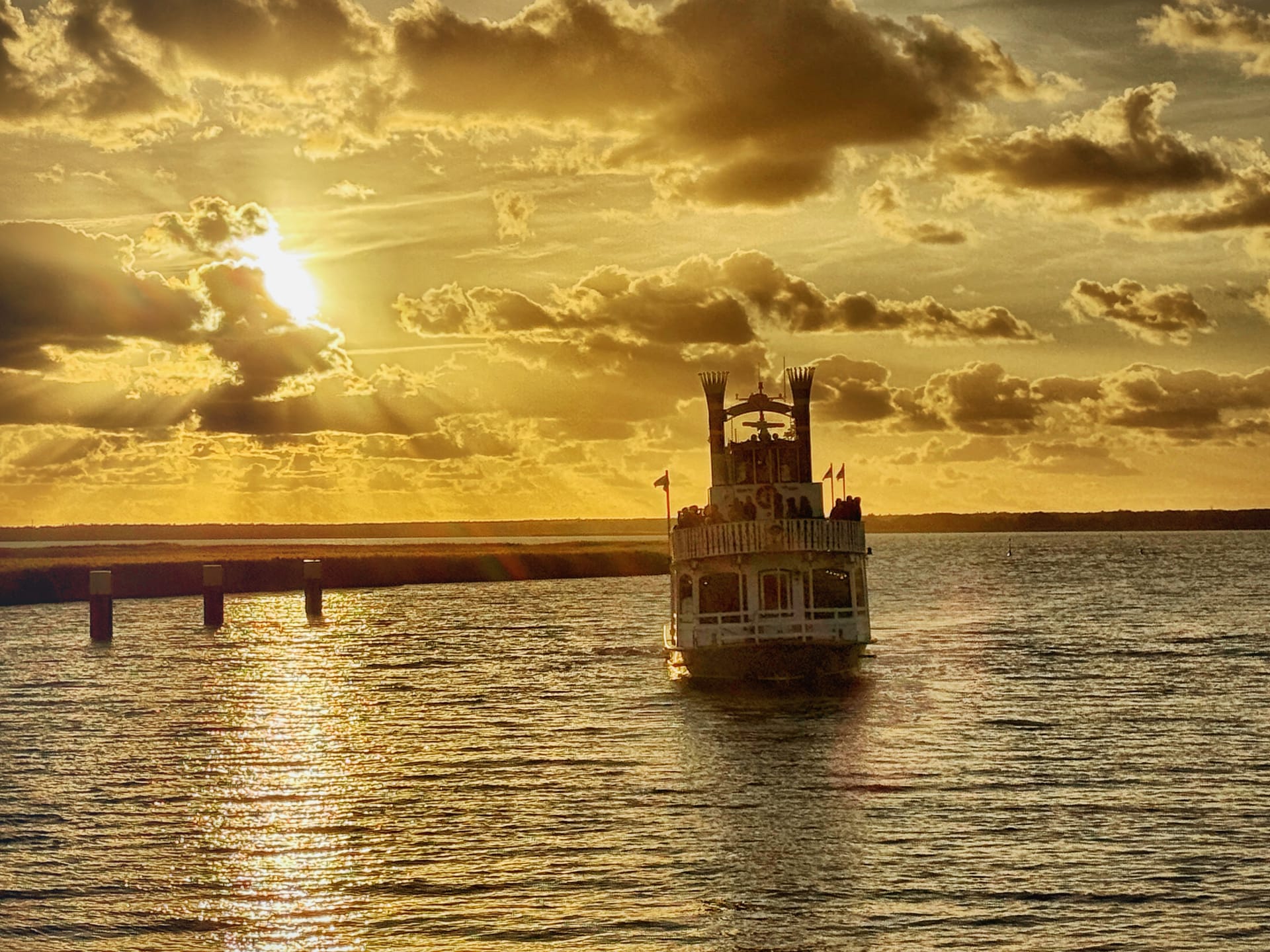 Schaufelraddampfer fährt bei goldenem Sonnenuntergang über ruhiges Boddenwasser.