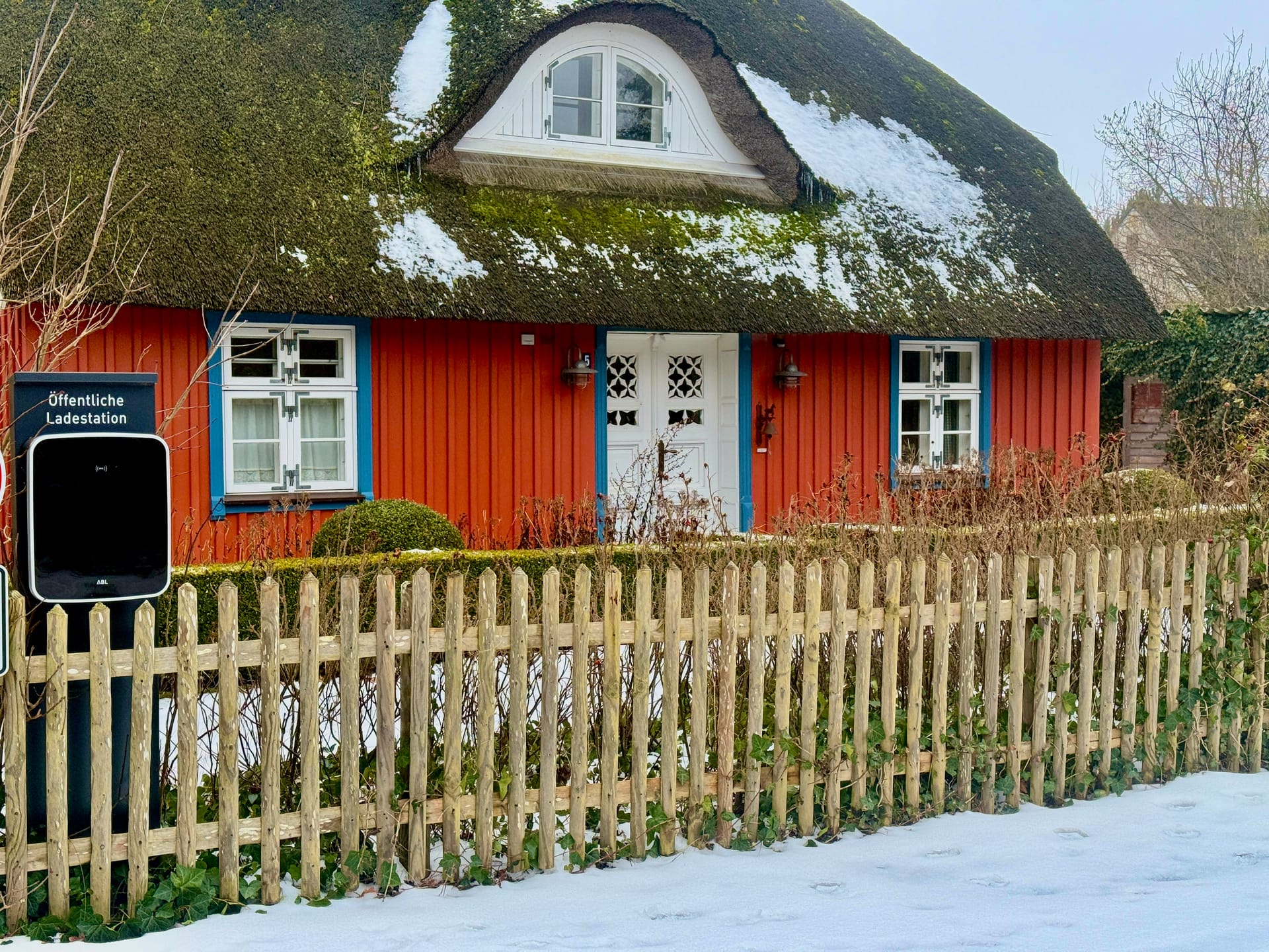 Reetdachhaus in Born im Winter mit Schnee und Holzzaun und E-Lade-Säule