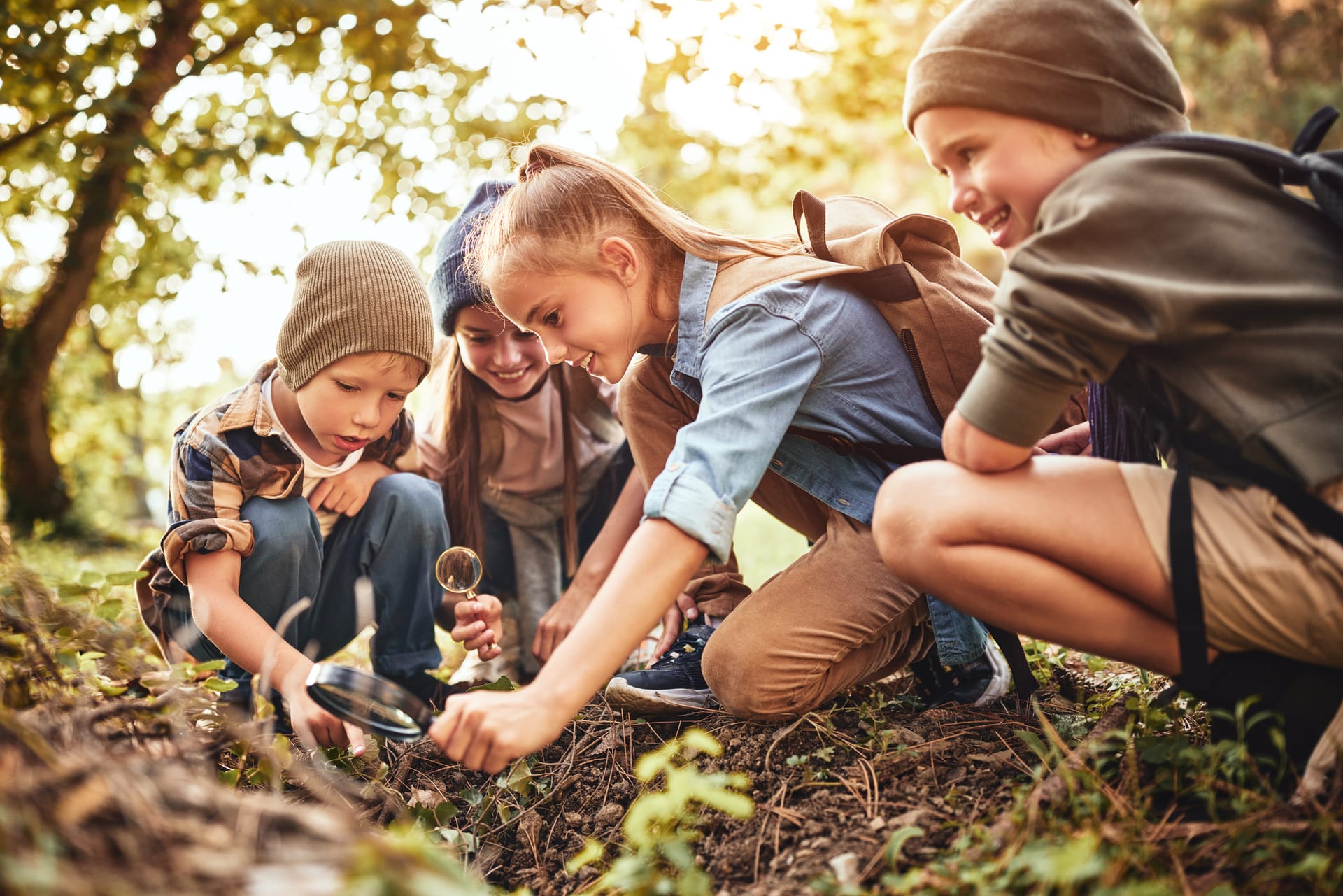 Kinder entdecken mit Lupen den Waldboden bei einem Ausflug in die Natur