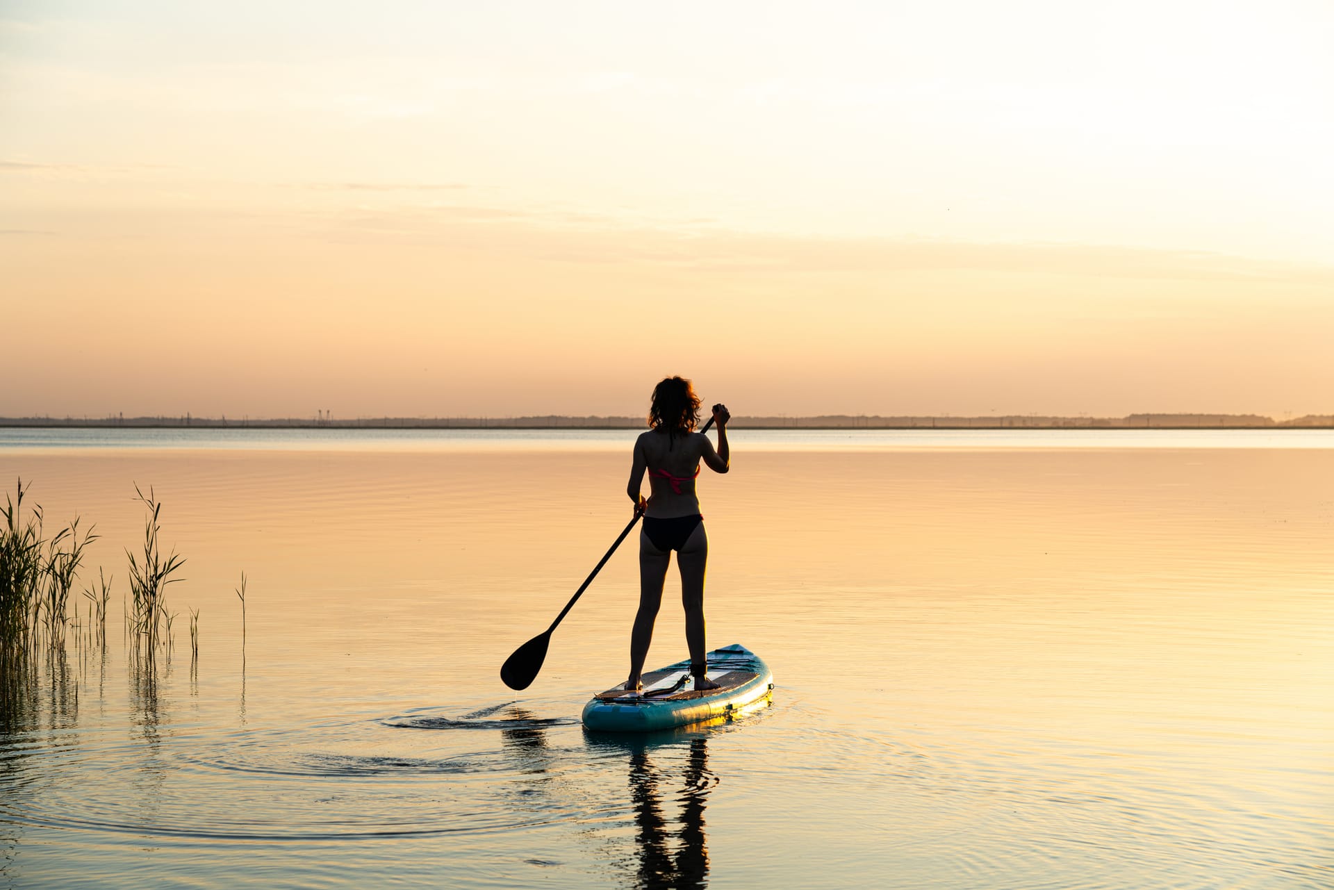 Stand-up-Paddlerin gleitet bei Sonnenuntergang über ruhigen Bodden