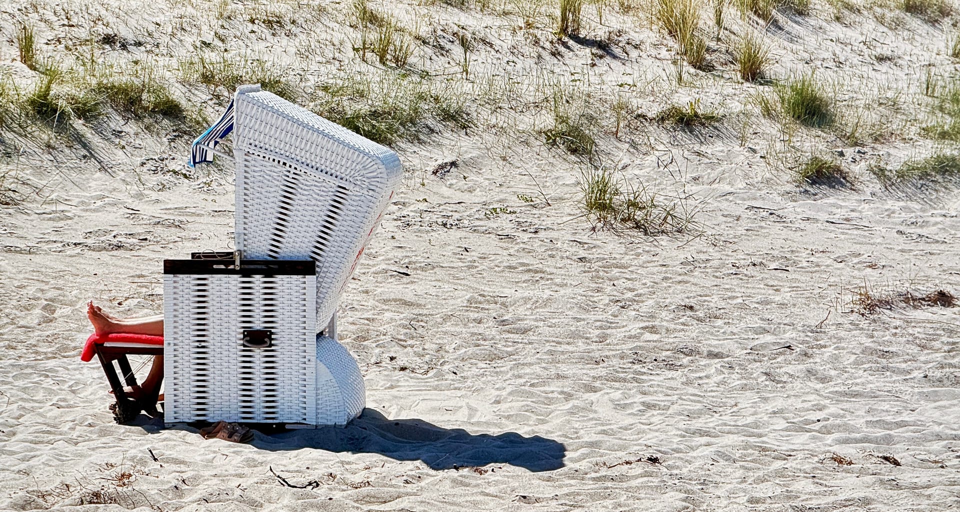 Weißer Strandkorb aus dem zwei nackte Beine rausgucken am Strand