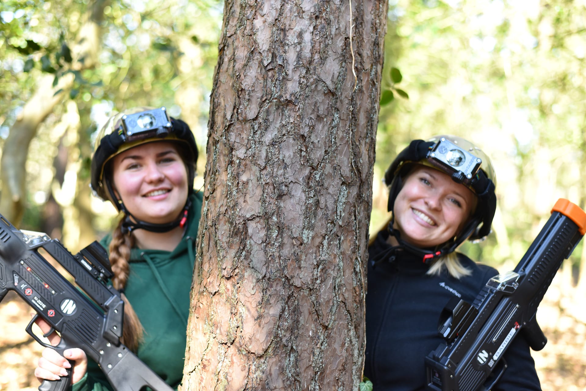 Zwei Frauen beim Lasertag im Wald hinter einem Baum in Deckung
