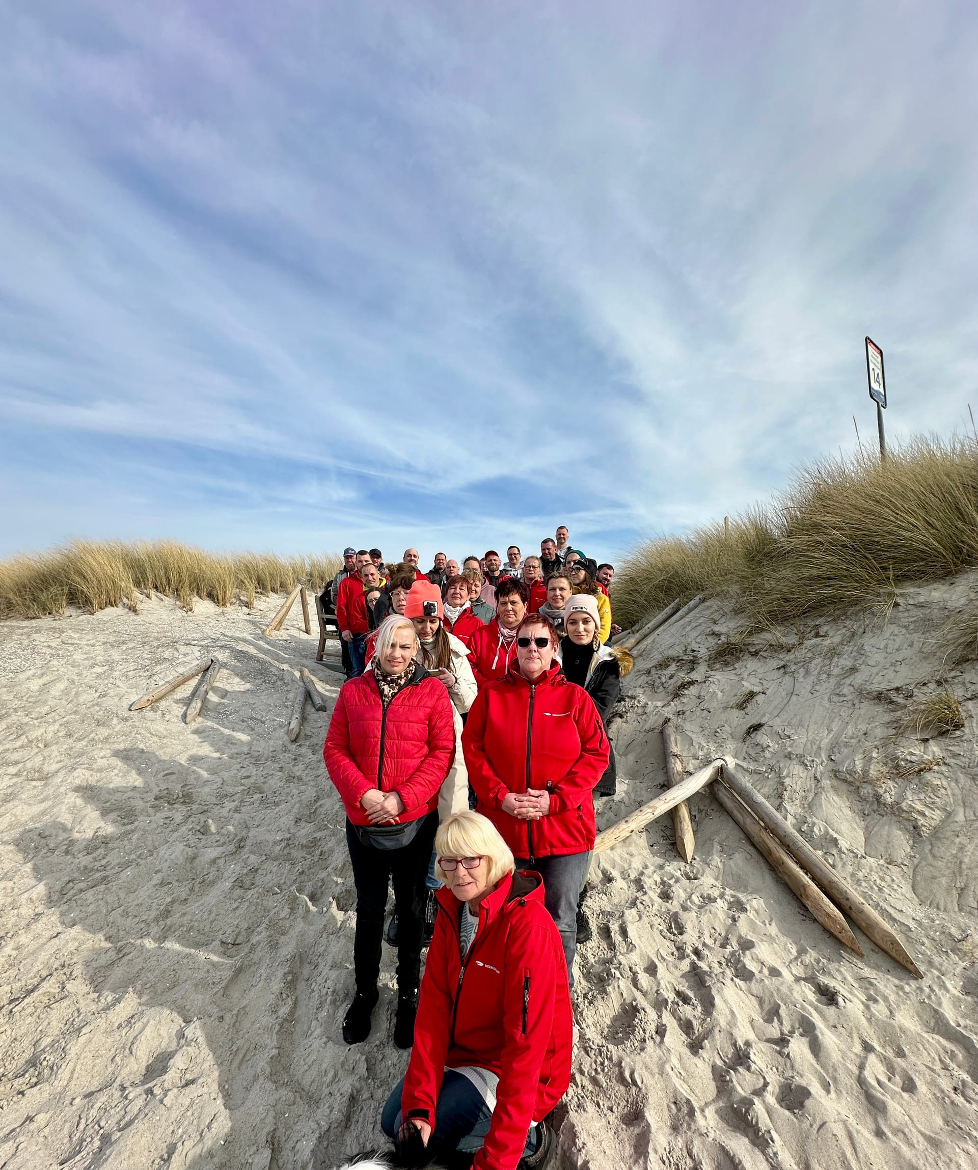 Gruppe in roten Jacken auf Dünenweg am Strand unterwegs