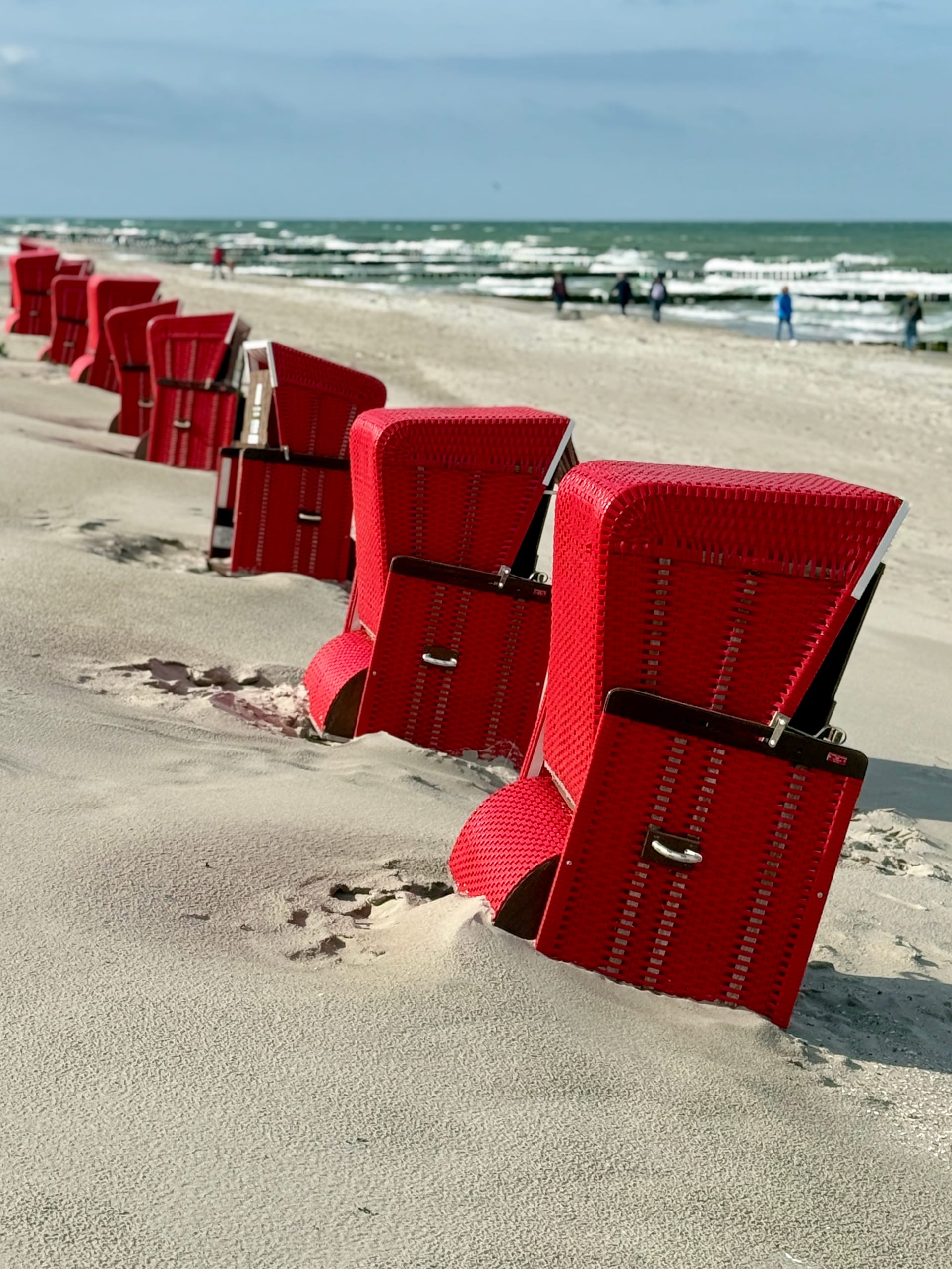 Rote Strandkörbe in Reihe am Ostseestrand bei windigem Wetter