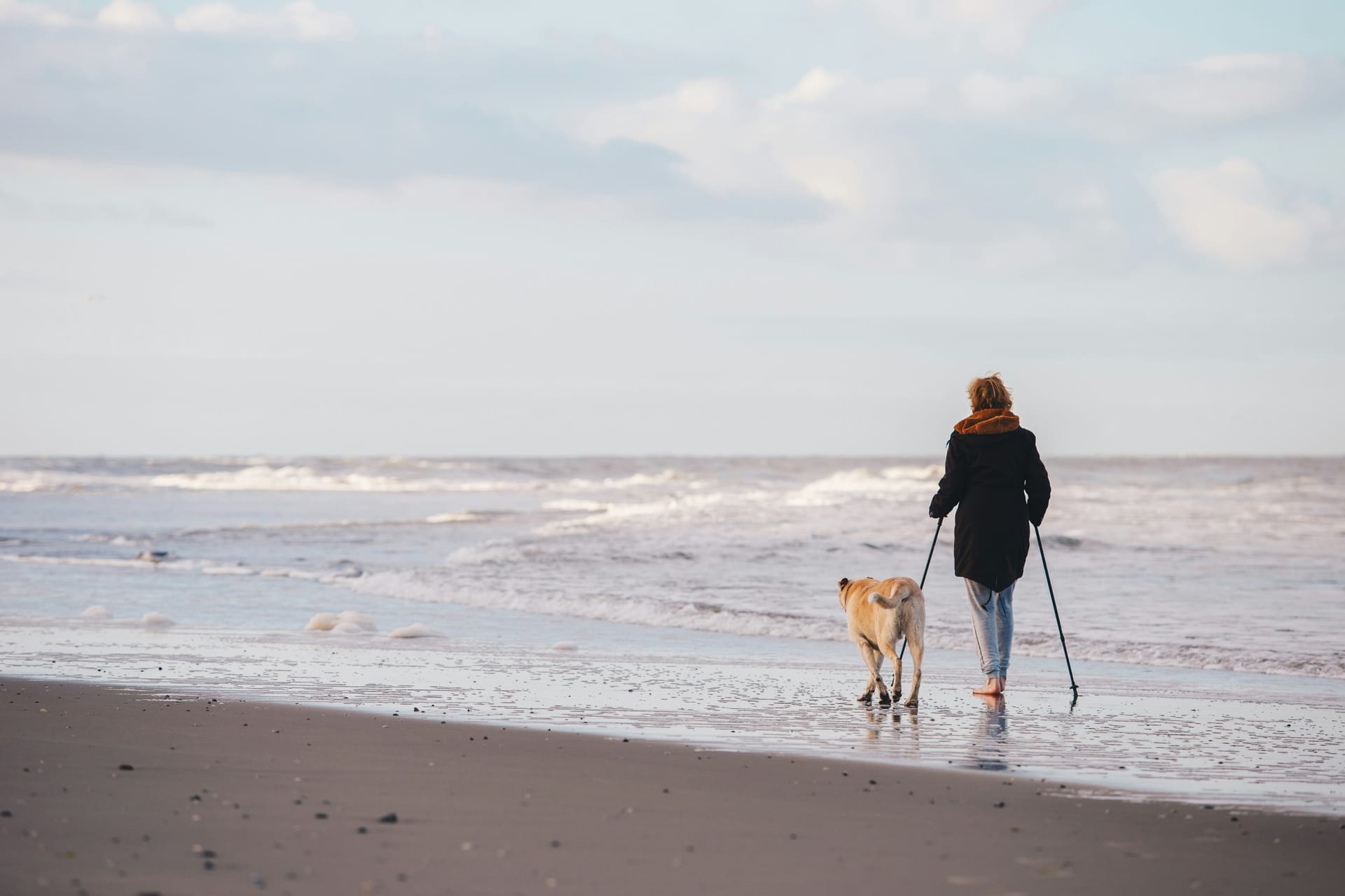 Frau geht mit Hund am Strand spazieren