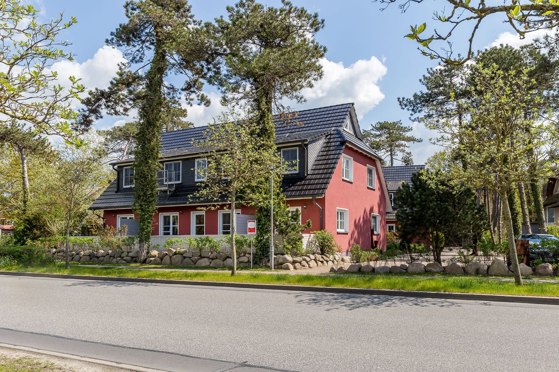 Außenansicht eines roten Hauses mit Bäumen und Parkplatz.
