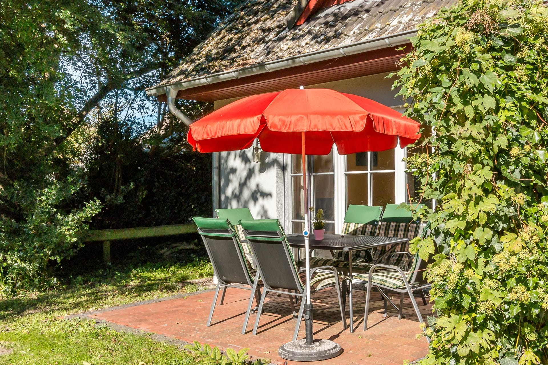 Terrasse mit Tisch und rotem Sonnenschirm