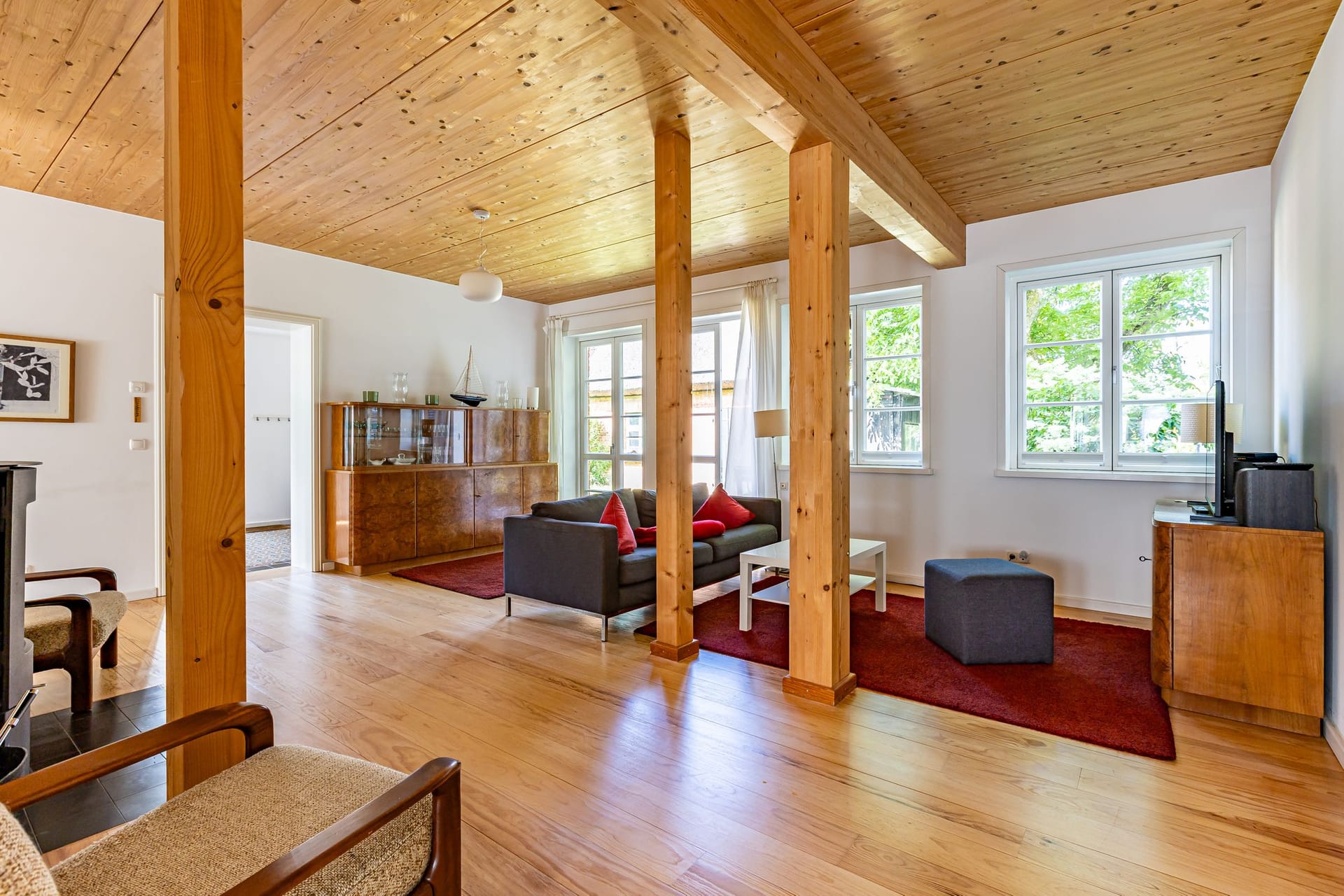 Gemütliches Wohnzimmer mit Holzdecke und großen Fenstern.