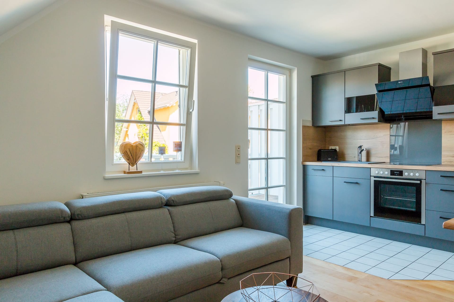 Wohnzimmer mit grauem Sofa und moderner Küche