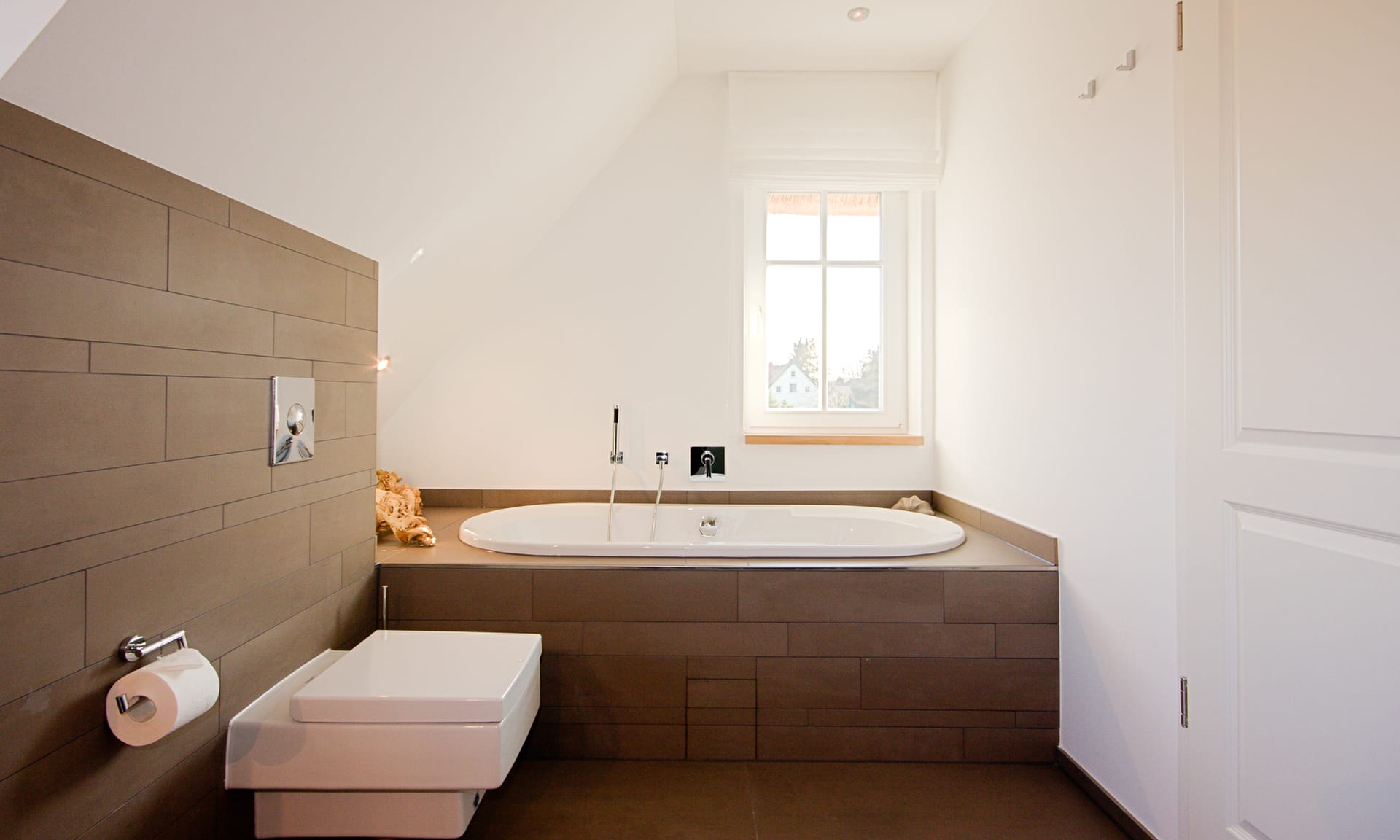 Badezimmer unter der Dachschräge mit Badewanne, wandhängendem WC und braunen Fliesen.