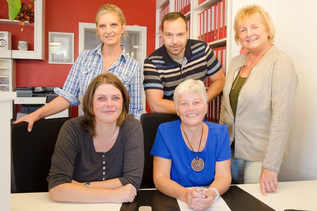 Mitarbeiter im Büro: lachend, zwei sitzend, drei stehend.