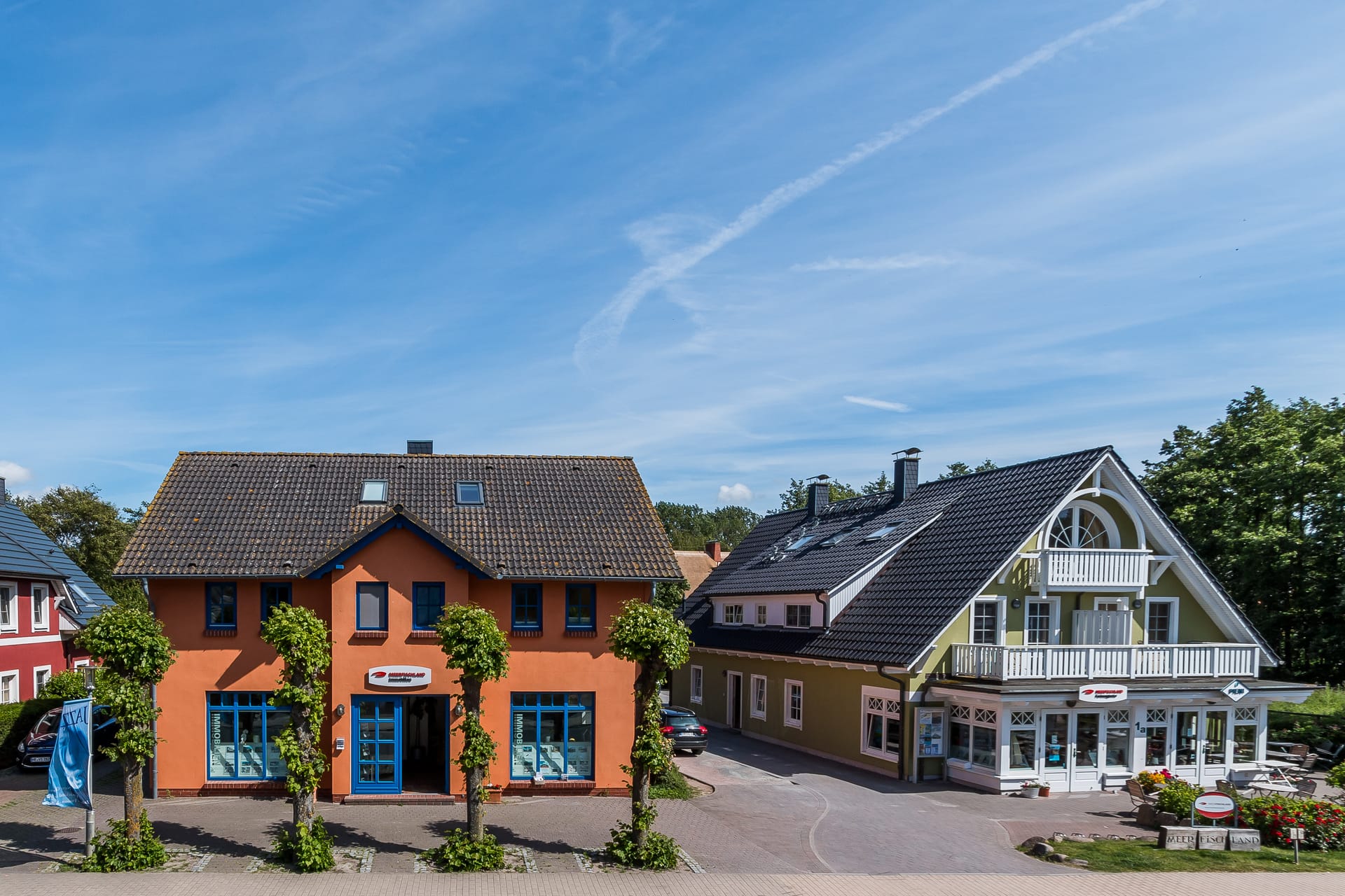 Zwei Gebäude: links orangefarbene Haus des Immobilienbüros Meerfischland, rechts das grüne Haus der Ferienagentur Meerfischland.