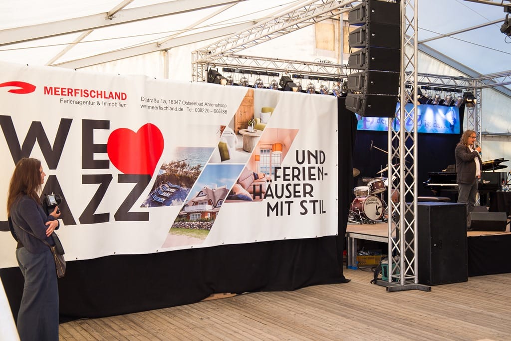 Ein Sprecher steht auf einer Bühne neben einem großen Werbebanner für das Jazzfest.