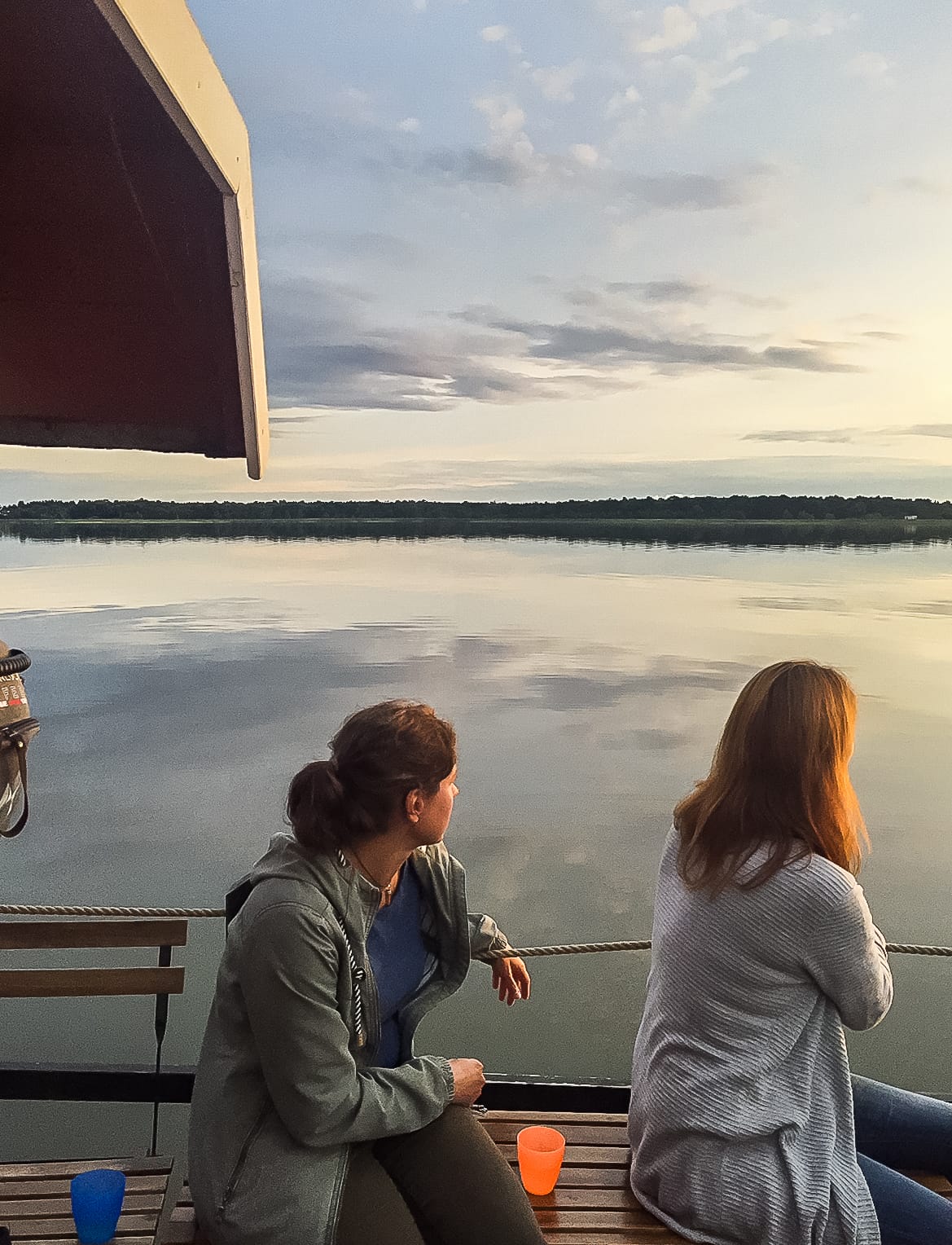 Zwei Frauen auf einem Floß am Wasser, in die Ferne blickend.