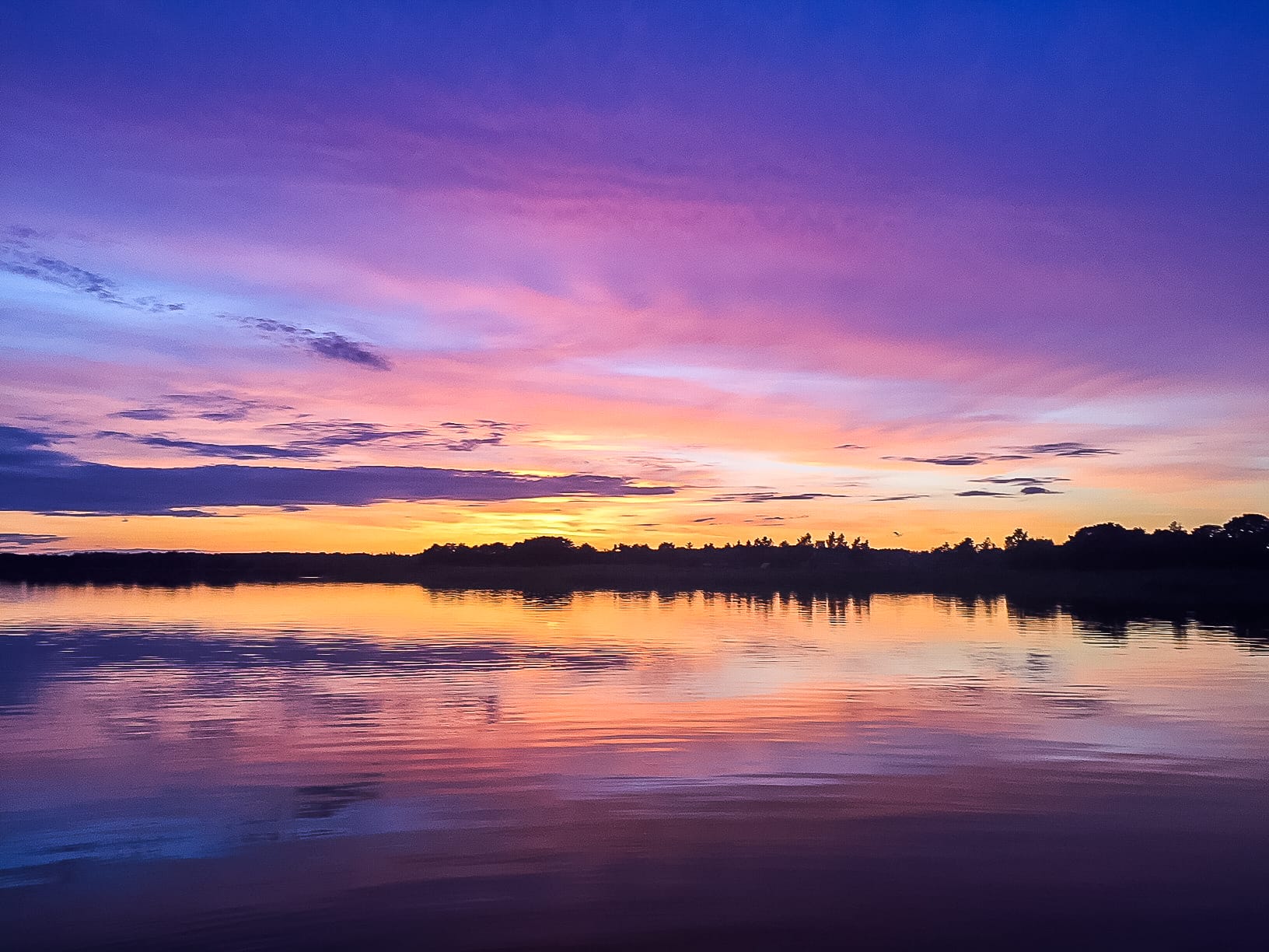 Bunter Sonnenuntergang über dem Wasser: Himmel in Blau, Rosa, Gelb und Violett.
