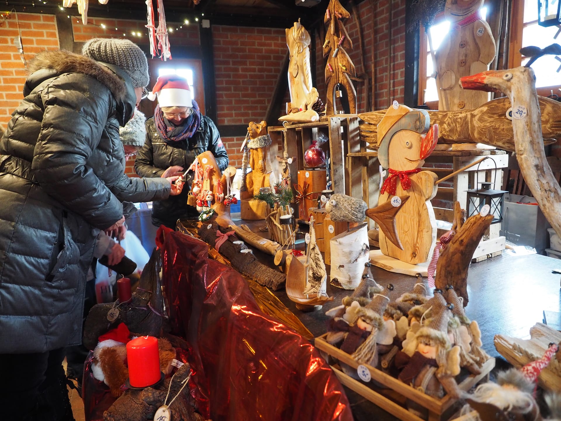 Holzfiguren und Dekorationen auf dem Tisch, zwei Frauen unterhalten sich, eine trägt eine Weihnachtsmannmütze.
