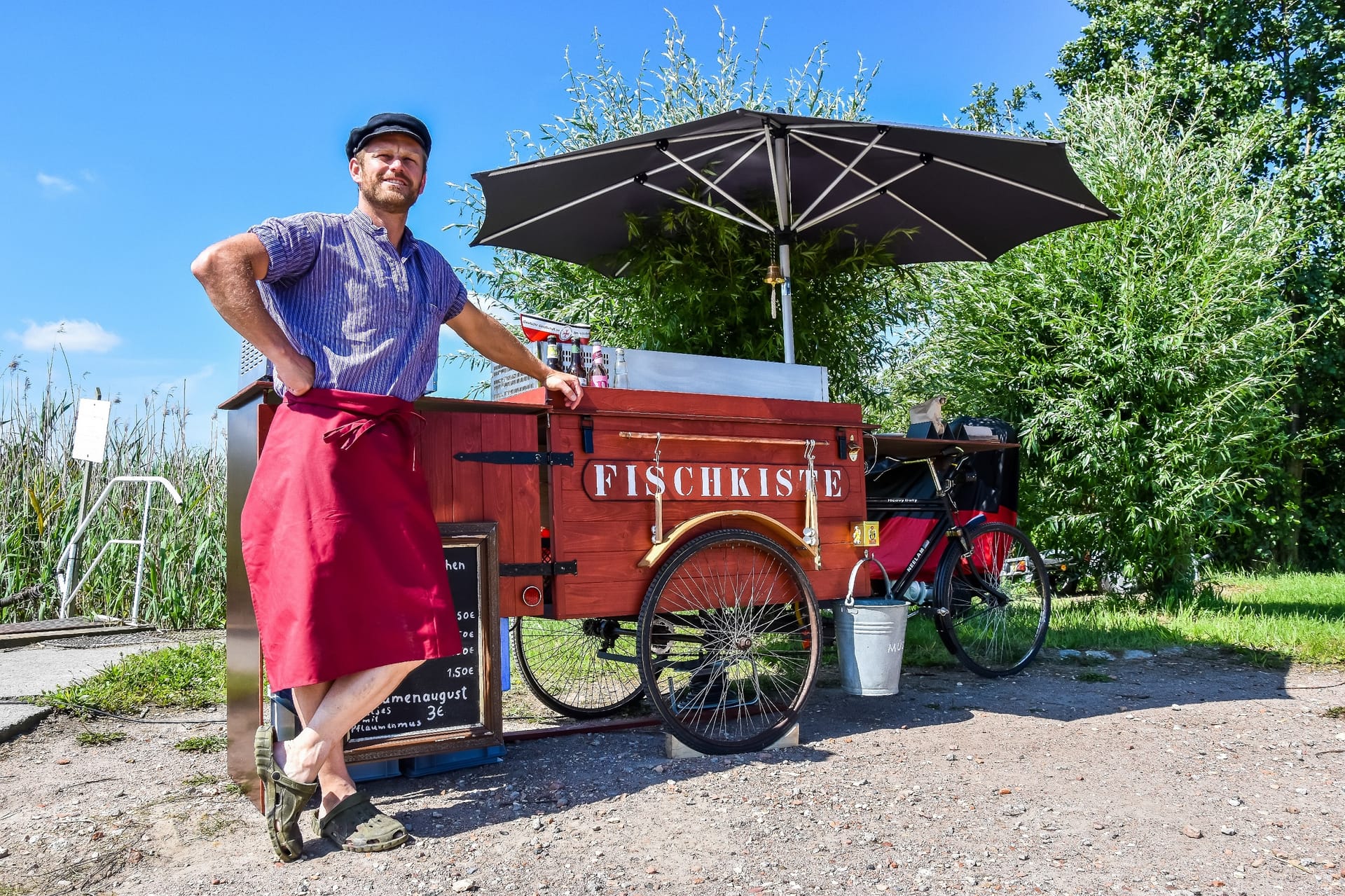 Ein mobiler Fischbrötchenstand namens „Fischkiste“ auf einem Lastenfahrrad mit Sonnenschirm und Verkäufer.